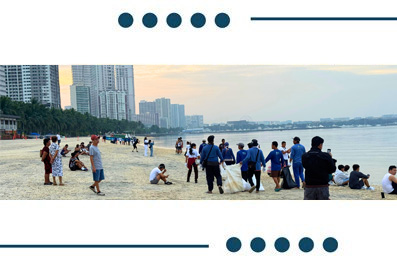 Busy city beach scene with people relaxing and playing on the sand, high-rise buildings across the water in the background.