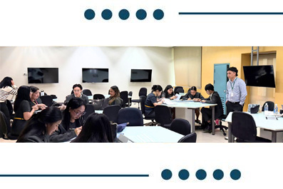 Group of adults in a classroom workshop around tables; instructor stands at front presenting.