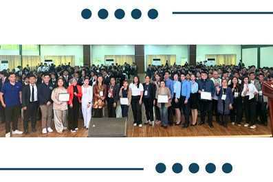 Large group of people in business attire posing for a group photo at a conference or ceremony; several participants hold certificates.