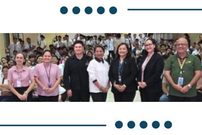 Diverse group of eight professionals posing for a group photo at an event, each wearing badges, in a crowded hall.
