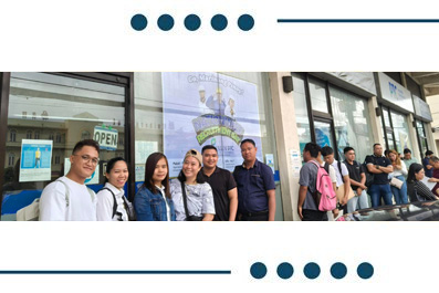 Group of people standing in a queue outside a storefront with glass windows and a poster on the door.