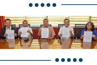 Five people seated at a conference table, each holding a signed document toward the camera.