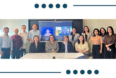 Group of professionals posing for a team photo in a conference room, with a video conference screen in the background.