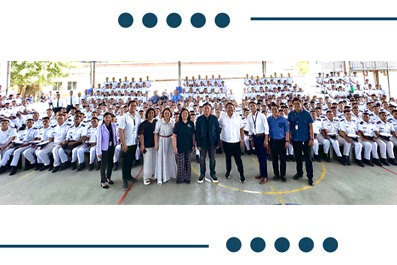 Large group photo of students in white uniforms with several adults standing at the front, posing in a gymnasium.
