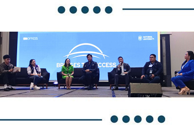 Seven panelists seated in a row on a stage during a conference, with a blue backdrop bearing logos and a circular design behind them.