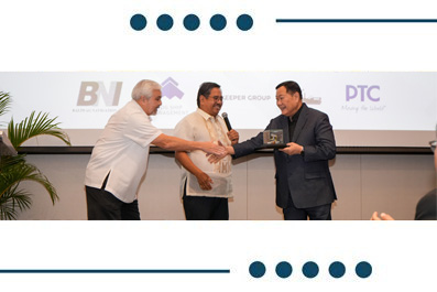 Three men on a stage during an award ceremony; the man in the middle receives a plaque from the man on the right while the man on the left reaches forward.