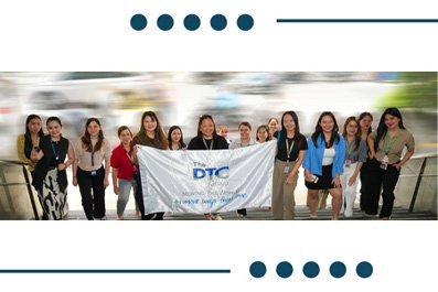 Diverse group of people posing outdoors behind a banner that reads DTC.