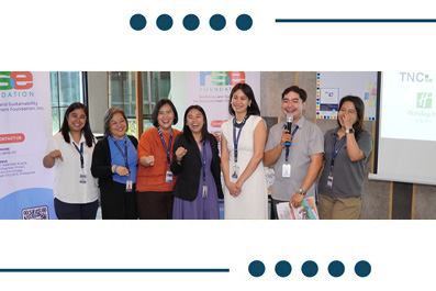Eight diverse presenters posing together at a conference, with banners and a projector screen behind them.