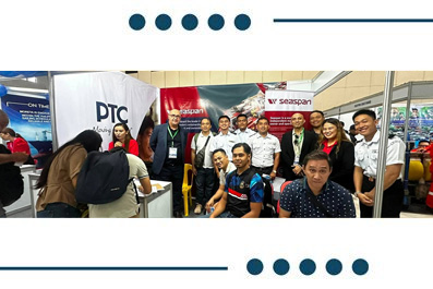 A diverse group of people posing for a photo at a trade show booth with company banners in the background.