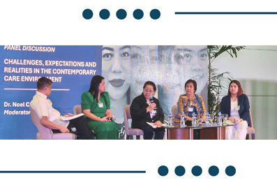 Panel discussion with five speakers seated on a stage, a moderator present, in front of a blue conference banner about challenges in contemporary care environments.