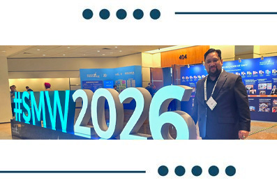 Man in a suit posing beside a large illuminated '#SMW 2016' sign at a conference hall with blue banners in the background