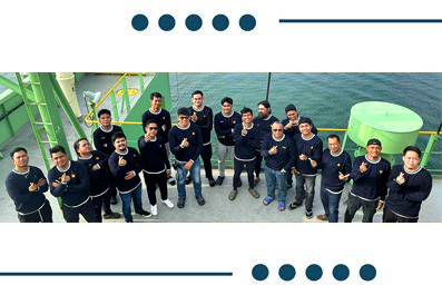 Group of about 16 people on a ship deck posing for a photo, giving thumbs up.