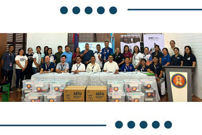 Group of volunteers posing with donation boxes and supplies at a community event, banners in the background, podium on the right.