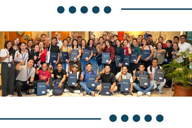 Group of diverse people posing with blue folders at a ceremony, indoors with a warm backdrop and crowding smiles.