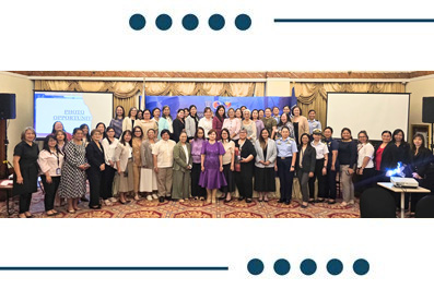 Group photo of event attendees posing on a stage in a conference room, with two screens visible on each side.