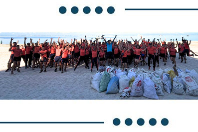 Large group of volunteers on a sunny beach posing behind piles of filled trash bags from a beach cleanup.