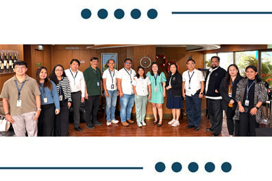 Group photo of about 16 diverse team members wearing badges, standing in a line in a conference room.