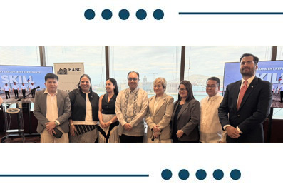 Nine professionals posing for a group photo at a conference, standing in a row with banners and windows behind them.