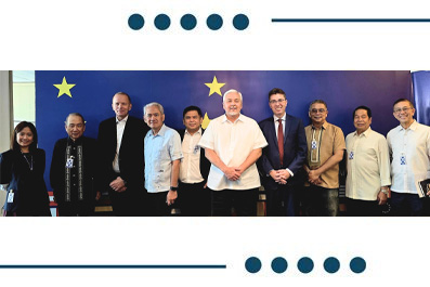 Group of twelve people in business attire posing for a formal photo in front of a blue backdrop featuring EU stars, at an international meeting.