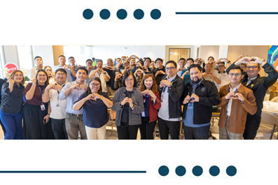 Diverse group of coworkers standing together in an office, forming heart shapes with their hands.