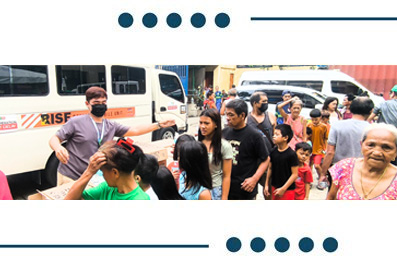 Diverse group of people waiting in a queue outside a white van; some wear masks, suggesting a public aid or health distribution scene.