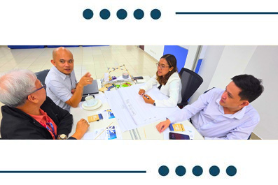 A group of four professionals seated around a table reviewing documents and discussing a chart or plan.
