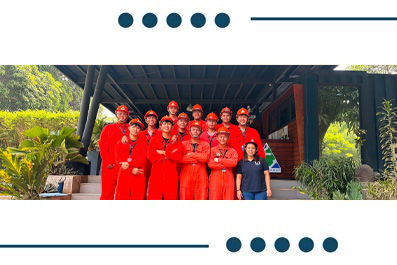 Team of workers in red coveralls and helmets posing for a group photo outside a wooden building.