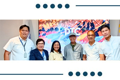 Five people standing together indoors in front of a colorful banner displaying 'PTC'.