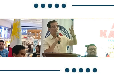 Man speaks into a microphone at a podium during a public event, with a Philippine flag and audience in the background.
